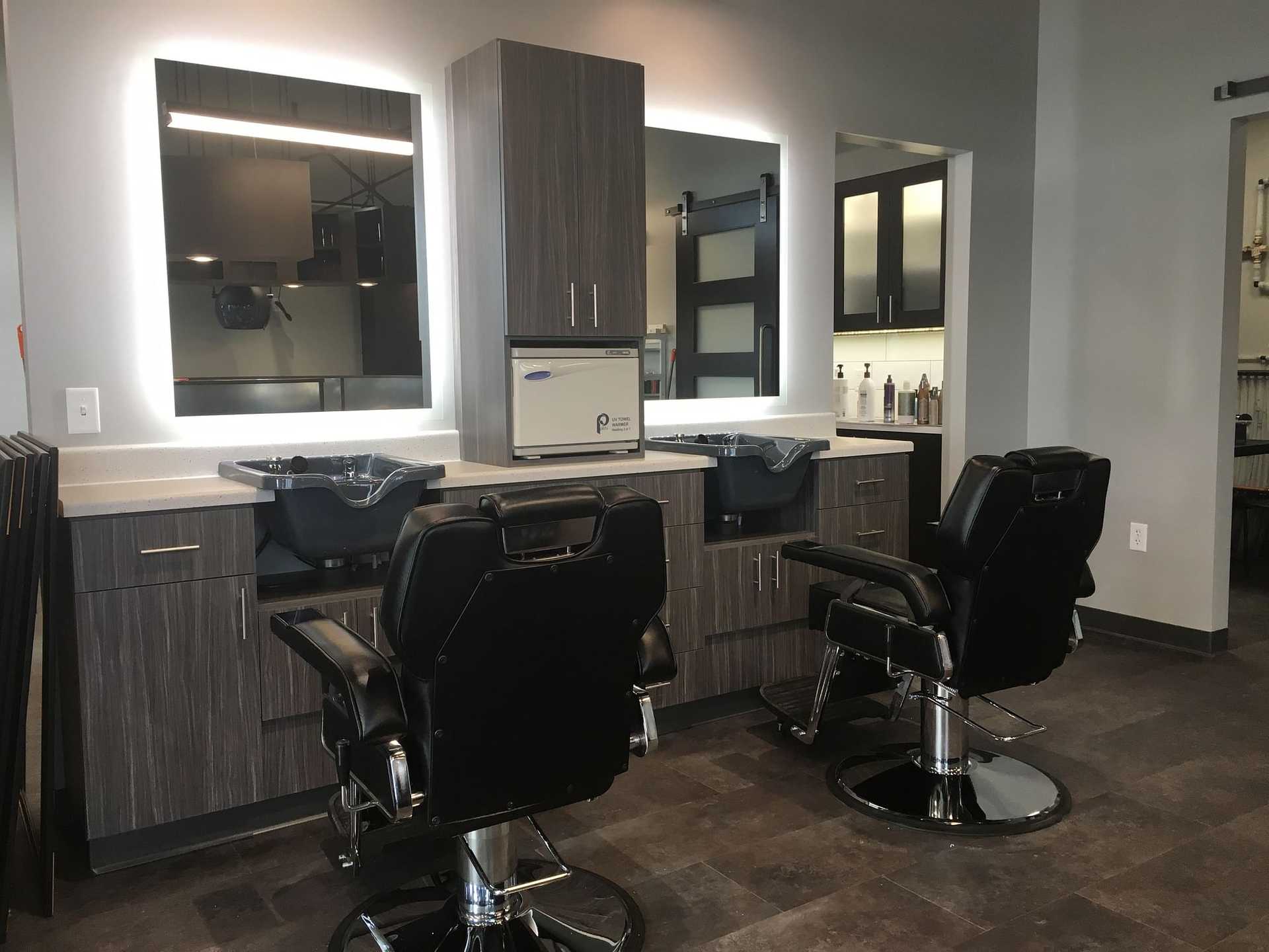 Modern hair salon with two styling stations featuring sleek wooden cabinetry and swivel chairs.