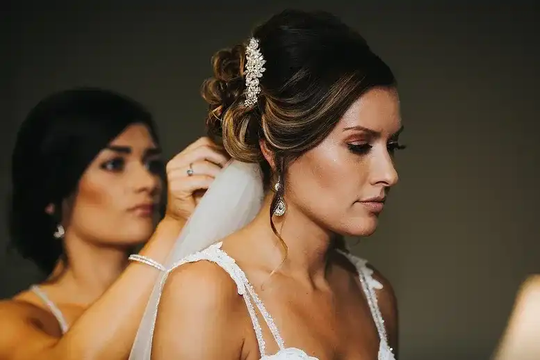 Bride preparing for her wedding with help from bridesmaid fixing her veil.