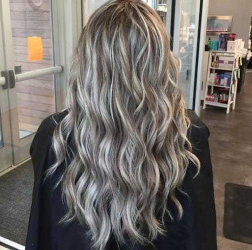 Woman with long, wavy, blond-highlighted hair in a salon setting.