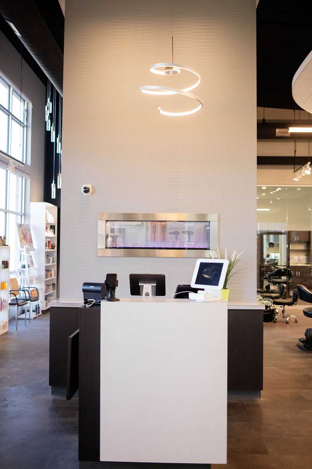 Modern salon reception with sleek desk, computer, and hanging spiral lighting fixture.