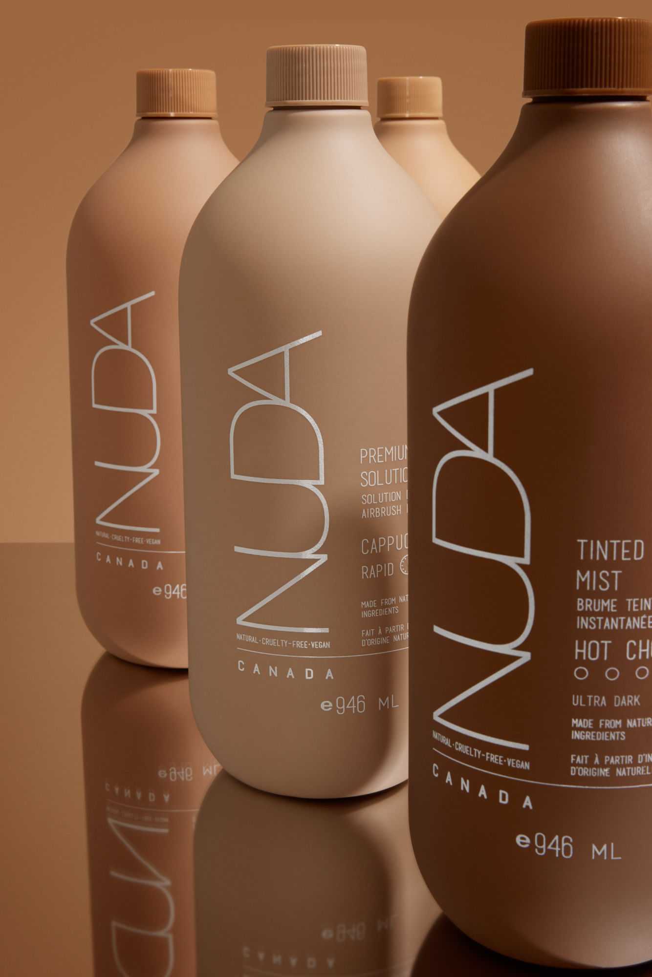 Bottles of NUDA tanning products in varying shades on a reflective surface.